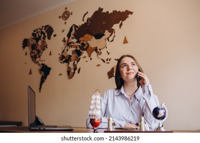 Beautiful Travel Agent Sitting At The Table In Office And Talking On Phone.