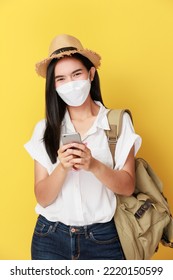 Beautiful Travel Asian Woman With Facemask Use Smart Phone Isolated On Yellow Background