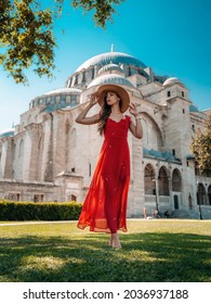 A beautiful travel blogger girl in a long red dress and a straw hat is photographed at the ancient sights in Istanbul in Turkey. The Blue Mosque of Suleiman in summer.