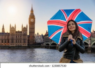 Beautiful traveler woman with Union Jack umbrella in front of the Big Ben clocktower in London; pretty urban tourist woman explores London during travel