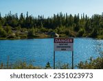 Beautiful tree-lined blue lake,  with cautionary contamination sign, sparkles in sunlight near Yellowknife, Northwest Territories, NT, Canada