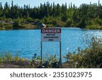 Beautiful tree-lined blue lake,  with cautionary contamination sign, sparkles in sunlight near Yellowknife, Northwest Territories, NT, Canada