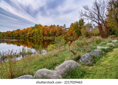 Beautiful Trees With Fall Foliage Lining Winding River With Boulders In Foreground