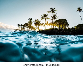 Beautiful Tropical Island Paradise Photo from Swimming In Clear Aqua Blue Ocean Water with Colorful Sky and Orange Clouds at Sunrise with Sun Rays Coming Through Bright Green Palm Trees in Maui Hawaii