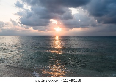 beautiful tropical landscape - with massive stormy clouds coming over water surface and sun reflecting in darker water surface with small black islands on a horizon, Bunaken Island, Indonesian sunset