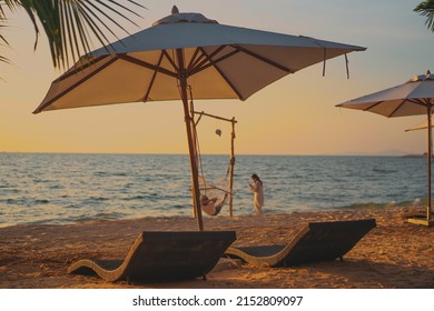 Beautiful Tropical Sunset Scenery, Two Sun Beds, Loungers, Umbrella Under Palm Tree. White Sand, Sea View With Horizon, Colorful Twilight Sky, Calmness And Relaxation With Couple Sweet On Background.