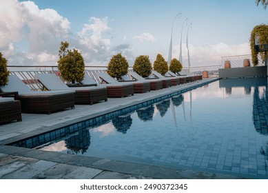 
Beautiful tropical swimming pool in hotel or resort with sun loungers, trees, with view of infinity pool, and clear cloudy sky in the morning - Powered by Shutterstock