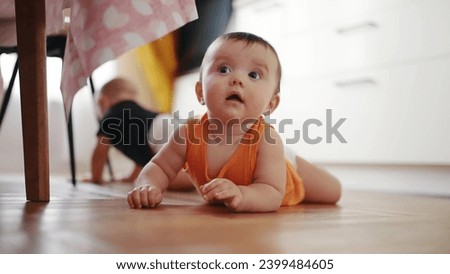 beautiful twin baby crawling under the kitchen table. carefree twins childhood. baby a boy funny crawling on the pope on the floor learning to crawl. Portrait twin of colorful fun baby crawling