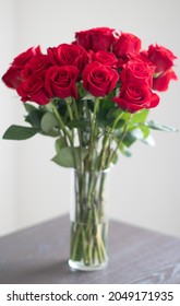 Beautiful Two Dozen Of Red Roses In A Clear Vase On The Table In A Room.