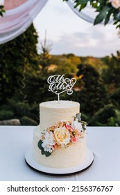 A Beautiful Two-tier Wedding Cake With The Word Mr And Mrs, Decorated With Flowers, Stands On A Table With A White Tablecloth. Food Photography.