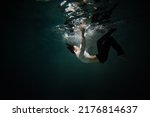 Beautiful underwater shooting, guy in white shirt and pants has fallen under the water and is drowning. a young man relaxes down under surface of the water, waves and refraction of light under water