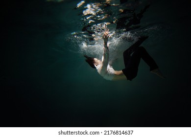Beautiful underwater shooting, guy in white shirt and pants has fallen under the water and is drowning. a young man relaxes down under surface of the water, waves and refraction of light under water - Shutterstock ID 2176814637