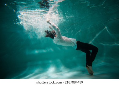 Beautiful underwater shooting, guy in white shirt and pants has fallen under the water and drowning. go to bottom, concept. young man paddles with his hands under water, waves and splashes around - Shutterstock ID 2187084439