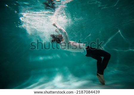 Beautiful underwater shooting, guy in white shirt and pants has fallen under the water and drowning. go to bottom, concept. young man paddles with his hands under water, waves and splashes around