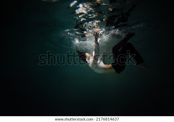 Beautiful underwater shooting, guy in white shirt\
and pants has fallen under the water and is drowning. a young man\
relaxes down under surface of the water, waves and refraction of\
light under water