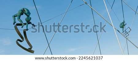 
Beautiful, unusual sculptures of aerial acrobats on a stretched wire with metal crossbars in the air above the bridge, against the blue sky.