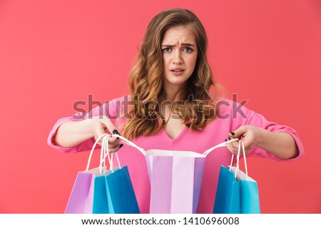 Beautiful upset young girl wearing casual clothes standing isolated over pink backgound, carrying shopping bags