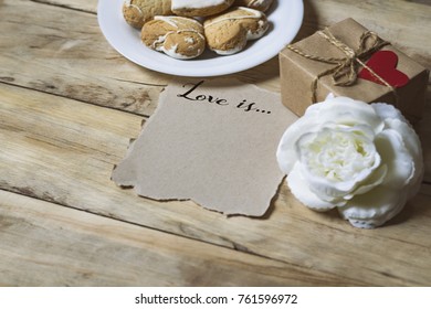 Beautiful Valentine's day concept. The inscription Love is ... A cookie in the form of a heart, a gift box with a heart and a white rose on a wooden background. - Shutterstock ID 761596972