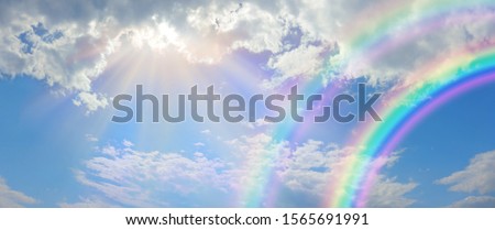 Beautiful vibrant double rainbow Cloudscape Background - awesome blue sky with pretty clouds, bright sun shining down and a large double rainbow arcing across the right corner with copy space
