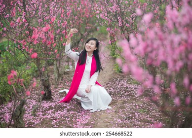 Beautiful Vietnamese girl with traditional dress (ao dai) is in peach flower garden in Hanoi, Vietnam