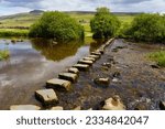 Beautiful view across the River Doe stepping stones with The Ingleborough mountain in the distance, which is at the halfway point along the Ingleton waterfalls trail, Ingleton, North Yorkshire, UK.