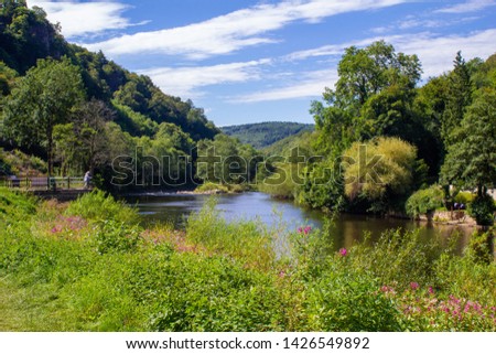 Beautiful view across the Wye river at Ross-On-Wye in Hereford, England. Sunny day with a still blue river and lush green trees and plants surrounding it either side.  