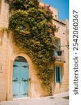 Beautiful view of ancient narrow medieval street with lanterns, colourful blue door and beautiful flower tree in the old town of Mdina on a sunny day, the silent city, ancient capital of Malta, Europe