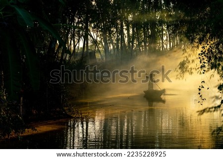 Beautiful view of an asian adult male old boatman rowing a wooden boat with a bamboo stick across a small river stream during sunset to deliver dry grasses for animal feeds in northeast Thailand