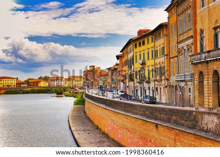 A beautiful view of buildings along the Arno river in Pisa, Italy. A bridge passes over the river and houses on both sides are overlooking the water