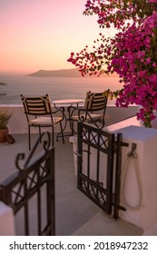 Beautiful view of Caldera and enjoying romantic scenery sunset Aegean sea, Santorini. Couple travel vacation, honeymoon destination. Romance with flowers, two chairs table and sea view. Luxury holiday