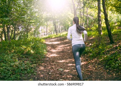 Beautiful View Of Caucasian Woman Runner Wearing Grey Leggings Doing Jogging Exercises Outdoors In Forest. Action Shot Of Female Jogger With Athletic Body During Morning Run. Healthy Motivation. 