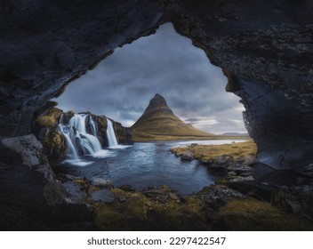 A beautiful view from a cave of a waterfall with river and Kirkjufell hill under cloudy sky in Iceland - Powered by Shutterstock
