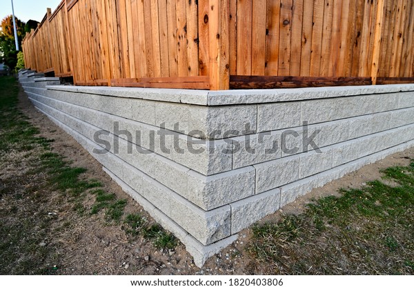 A beautiful view of a corner\
section of gray block retaining wall with a fence build\
behind