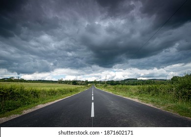 A beautiful view of an empty road surrounded by greenery under dark storm clouds