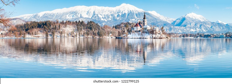 Beautiful view of famous Bled Island (Blejski otok) at scenic Lake Bled with Bled Castle (Blejski grad) and Julian Alps in the background in golden morning light at sunrise in winter, Slovenia.