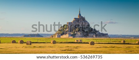 Beautiful view of famous historic Le Mont Saint-Michel in golden evening light at sunset in summer with hay bales on fields with retro vintage Instagram style pastel filter effect, Normandy, France