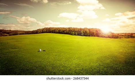 Beautiful View Of Green Golf Field With Ball And Hole At Sunrise In The Morning. Hobby, Leisure And Activity Concept. Golf Ball On Lip Of Cup.