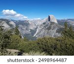 Beautiful view of Half Dome in Yosemite National Park, surrounded by green forests and a clear blue sky with a few clouds.