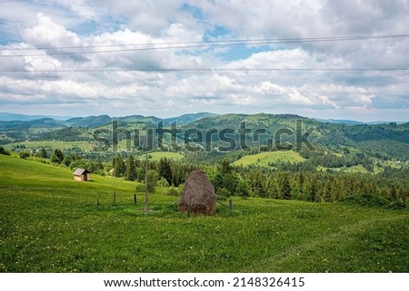 Beautiful view of haystack and old house on green slope of field against beautiful mountain ranges and cloudy sky