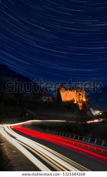 Beautiful view of Italian\
castle with trails of stars and car lights - snow covered Alps in\
background