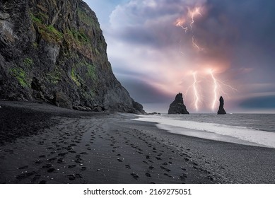 Beautiful view of lightning at Reynisfjara Beach. Footprints on black sand seashore against cloudy sky. Scenic view of cliff at famous tourist attraction during stormy night.