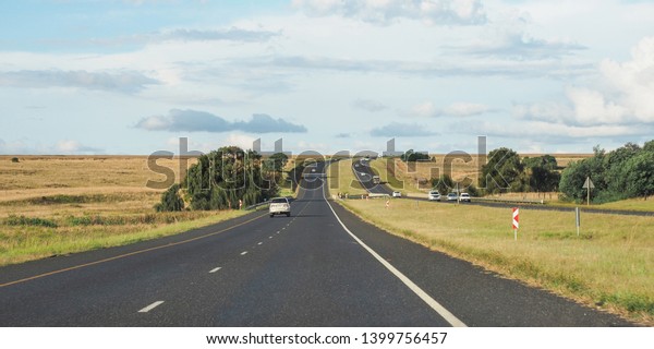 Beautiful view of long road from inside the car\
through the window. Empty long road with nice green grass on both\
side with sky full of\
cloud
