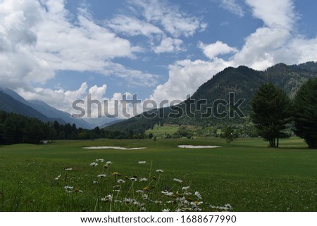 A beautiful view of lush green golf course sourrended by beautiful hills with pine trees at Pahalgam Kashmir,India.