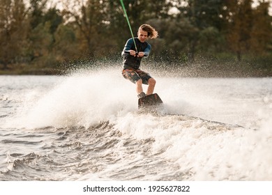 Beautiful view of man holding bright cable in his hands and balancing on wakeboard on wave.