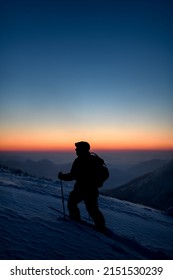 beautiful view of man in ski suit with ski poles on deep powdery snow against the backdrop of sunset sky and mountain peaks