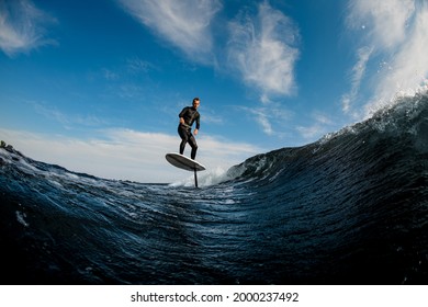 Beautiful view of man skillfully riding on the wave with hydrofoil foilboard on background of blue sky