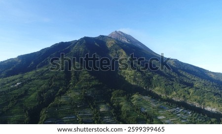 beautiful view of Mount Merapi. The mountain, a volcano, has a prominent peak with green vegetation covering its slopes. The foreground features terraced gardens, adding to the natural beauty.