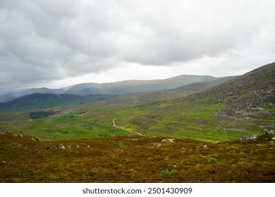 A beautiful view from a mountain overlooking a lush green valley, with a winding road cutting through the landscape. A dramatic grey sky looms above, adding intensity to the rugged, Scotland, UK. - Powered by Shutterstock