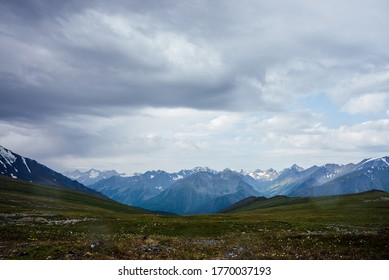 Beautiful view from mountain pass to great snowy mountains under cloudy sky. Dramatic alpine landscape with snow mountains in rainy weather. Gloomy scenery with giant mountain ridge in overcast day. - Powered by Shutterstock