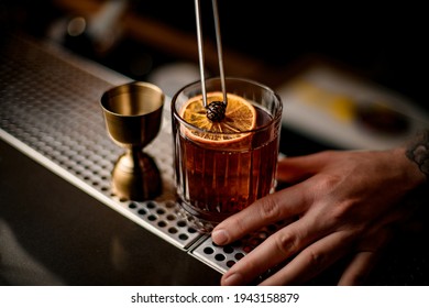 beautiful view on old-fashioned glass with cold alcoholic cocktail decorated with orange slice and small pine cone
